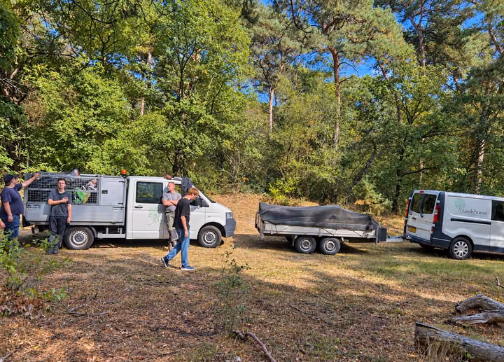 Deelnemers en begeleiders bij de bus en de aanhanger van Lindehoeve, aan het werk in het bos