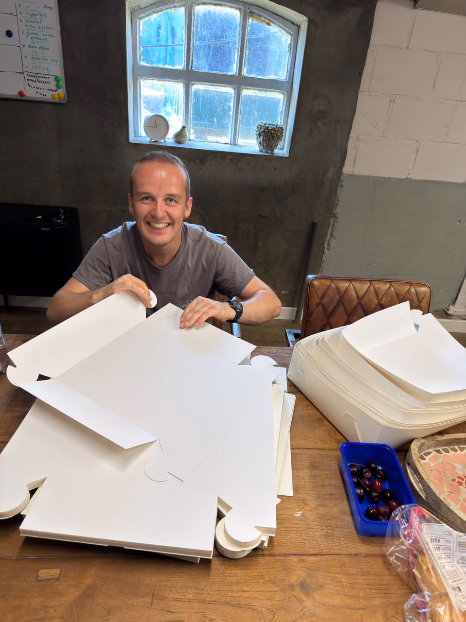 Een deelnemer vouwt lachend taartdozen aan een grote houten tafel