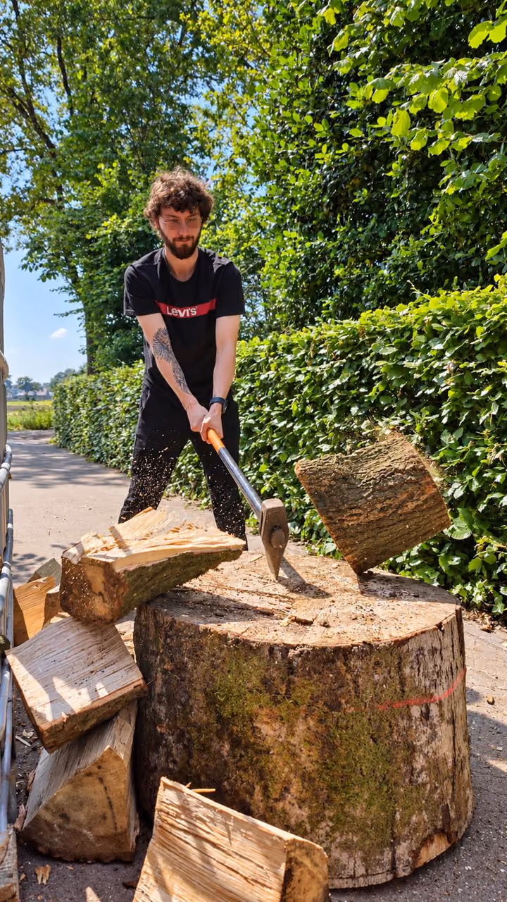 Een deelnemer klooft met een bijl een houtblok op een boomstronk, het blok valt uit elkaar