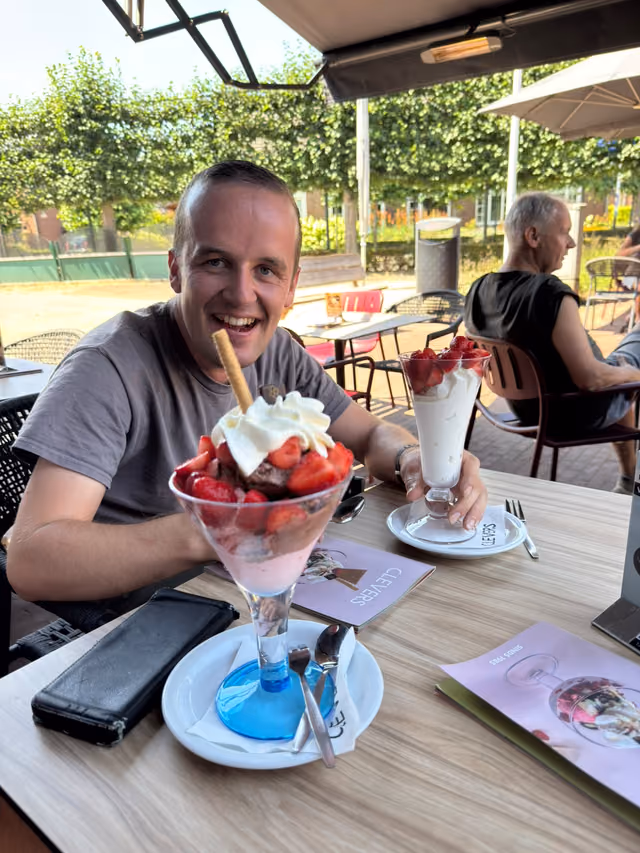 Een deelnemer lacht breed met een grote ijscoupe op een terras
