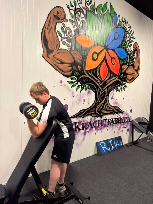 Een deelnemer traint met een halter in de Krachtfabriek, voor de muurschildering met de boom