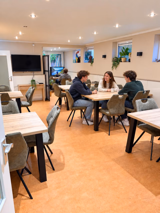 Een lichte ruimte met tafels en stoelen waar drie jongeren samen zitten