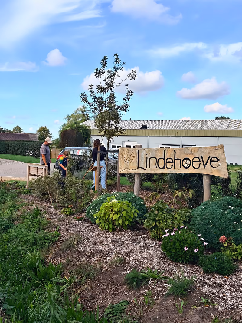 Medewerkers en deelnemers samen buiten bij het Lindehoeve-bord