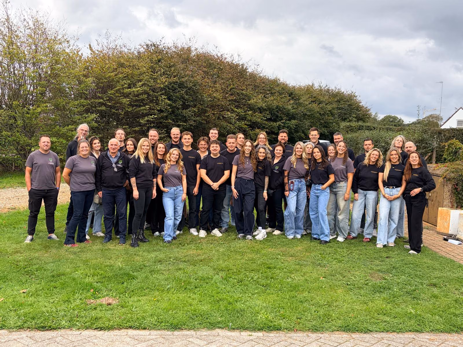 Het voltallige team van Lindehoeve staat samen op het gras voor een grote haag, de meesten in shirts met het Lindehoeve-logo