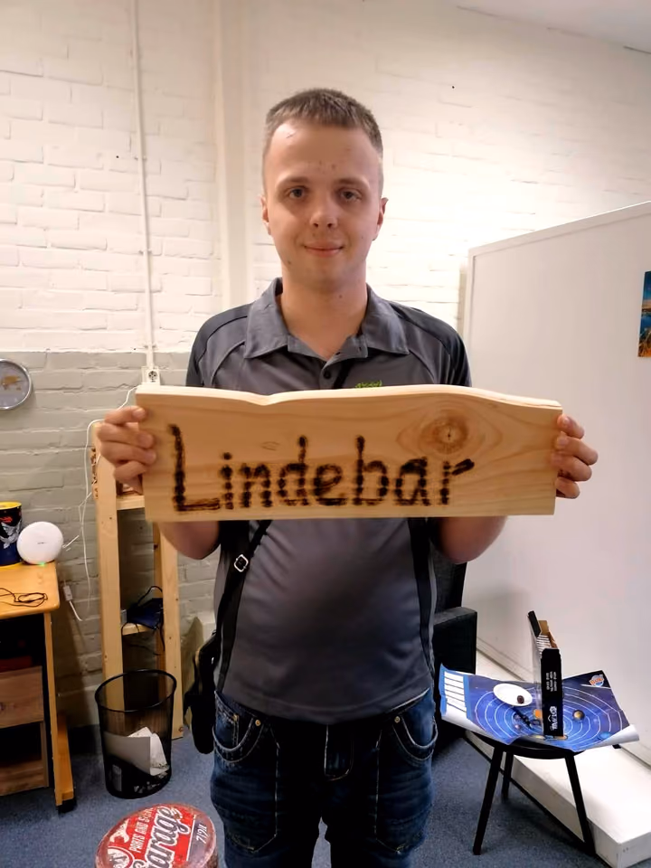 Een deelnemer houdt trots het houten bord omhoog dat hij heeft gemaakt, met de ingebrande naam Lindebar